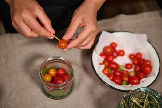 Overhead view of a housewife in black chef's apron pickling ripe and juicy cherry tomatoes at home kitchen