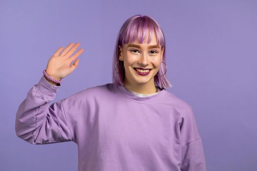 Friendly woman waving hand - goodbye, chao, adios. Parting, say bye to camera. Beautiful trendy girl with violet hairstyle waving hand on studio background.