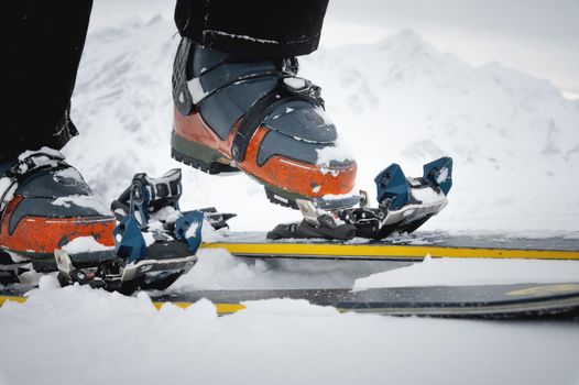 Close-up of the legs of an athlete-skier in ski boots against the backdrop of snow-capped mountains. The concept of winter extreme sports. Detail view of ski bindings and boots, all in motion