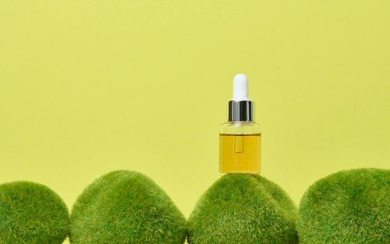 Glass transparent bottle with pipette and yellow oil on green moss.