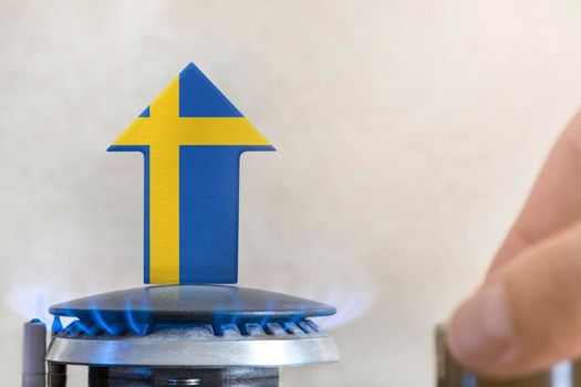 Gas price. Rise in gas prices in Sweden. A burner with a flame and an arrow up, painted in the colors of the Sweden flag. The concept of rising gas or energy prices.