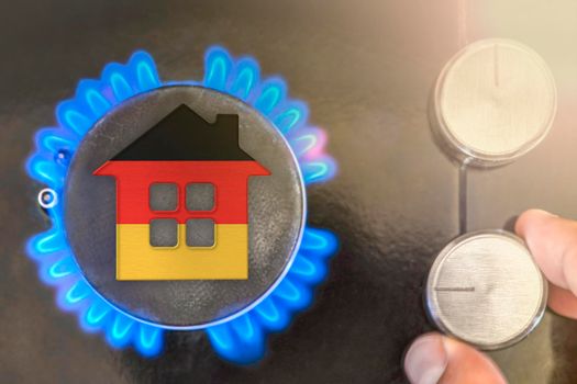 Heating season or gas use in Germany. Concept, model of a house stands near the flame of a gas boiler on a black background. The cost of using natural gas in Germany.