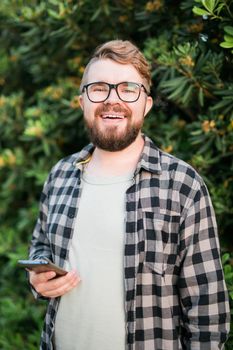 Portrait of attractive cheerful guy using smartphone for scrolling on social media over green tree background