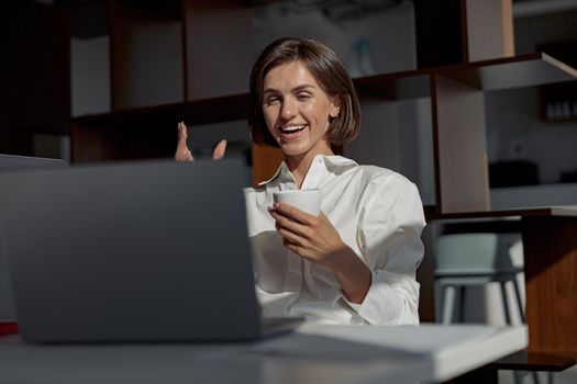 Businesswoman making video call to friends and showing sign V while working in modern office