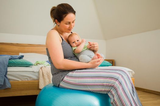 Mother holding and rocking baby sitting on fitball. New lifestyle with asleep newborn at bedroom