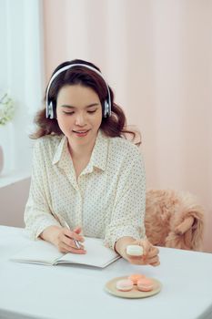 Peaceful asian woman wearing headphone and writing her diary.