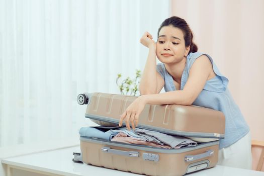 Sad young woman packing suitcase at home. Travel concept