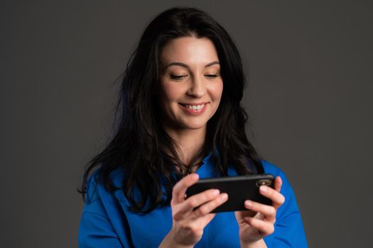Mature woman sms texting, using app on smartphone. Pretty adult lady surfing internet with mobile phone. Grey studio portrait.