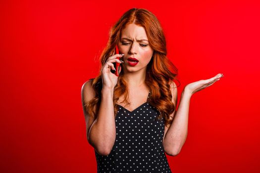 Woman with pretty appearance sort things out, swears with somebody by mobile phone. Girl nervous, expresses discontent, resentment. does not understand what happening. Red studio background