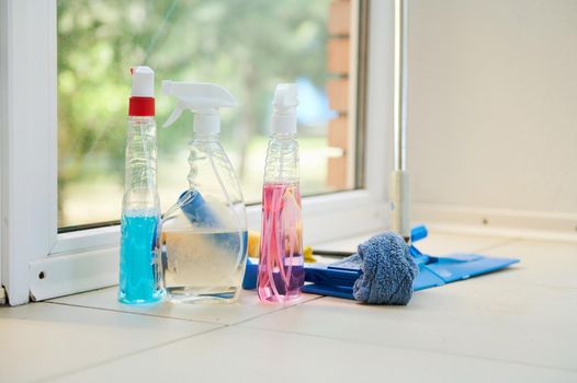 Cleaning products, household chemicals, detergents, rags and mop on the floor against panoramic window background.