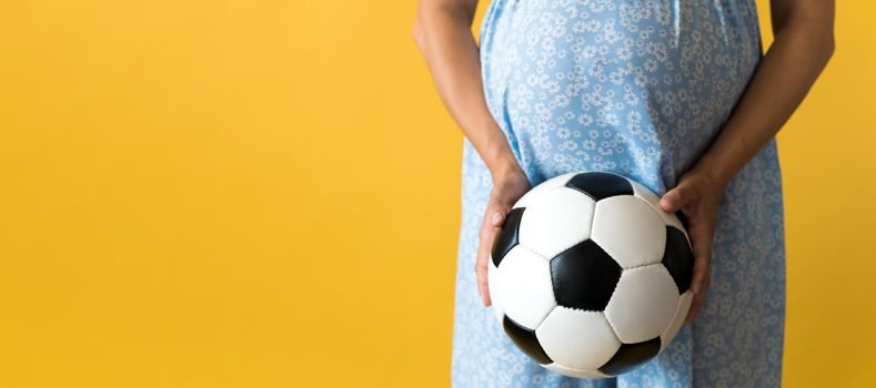 Motherhood, femininity, football, sport, dairy, hot summer. banner pregnant young pretty woman in floral blue dress holds soccer white and black leather classic ball rubs tummy on yellow background