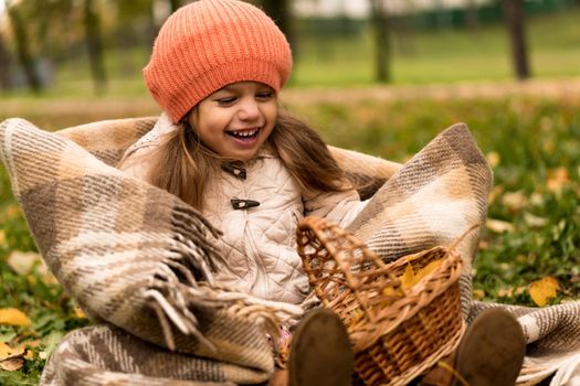 Little Cute Preschool Minor Girl In Orange Beret On Plaid At Yellow Fallen Leaves Basket Laughs Nice Smiling Look At Camera In Cold Weather In Fall Park. Childhood, Family, Motherhood, Autumn Concept