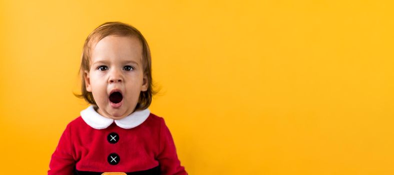 Banner Portraite Emotion Cute Cheerful Chubby Baby Girl in Santa Suit Yawns As If Singing At Orange Background. Child Christmas Scene Celebrating Birthday. Kid Have Fun Spend New Year Time Copy Space.