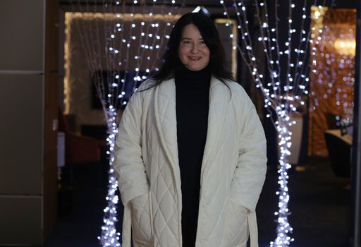Pretty brunette plus size woman in white coat in front of garlands.