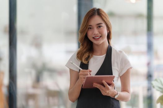 Beautiful Asian women Barista smiling and using tablet at her cafe