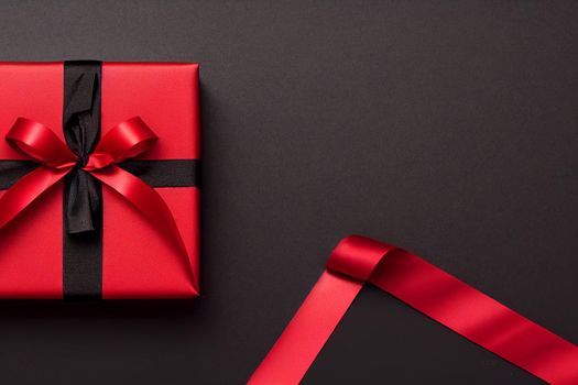 3D Render of red color gift box with black ribbon isolated against black background and Christmas decorations, top view design