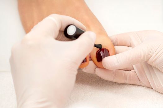 Pedicurist applying burgundy nail polish