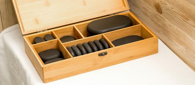 Close up of an open wooden case with spa black stones on a table in spa salon