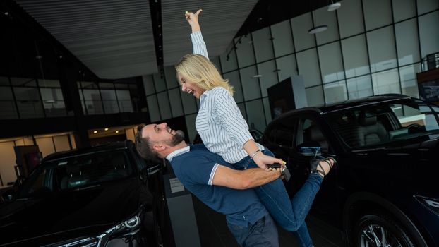 Happy caucasian couple hugging while buying a new car in a car dealership.