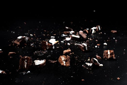 Scattered crumbs of chocolate sandwich cookies filled with sweet cream flavored isolated on black background.