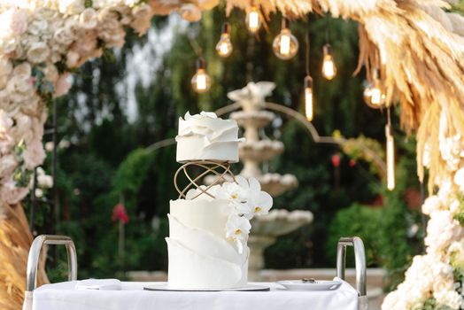 White wedding cake with flowers. Wedding cake on the background of the wedding arch