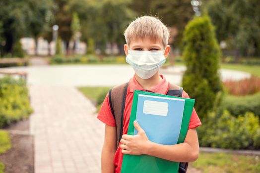 Small boy with backpack and protective mask in the park on the way to school