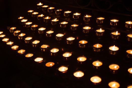 Rows of lighted prayer candles in the darkness in a church