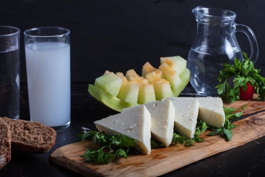 Turkish Raki with water on table with sliced melon and appetizer, traditional Turkish alcohol known as Raki, chill with friends at restaurant, dinner idea, eating and drinking concept, sitting view