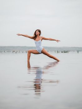 Young caucasian woman in swimsuit practicing yoga in water liman, lake or river. Beautiful reflection. Complex asanas, balance. Fitness, sport, yoga and healthy lifestyle concept.
