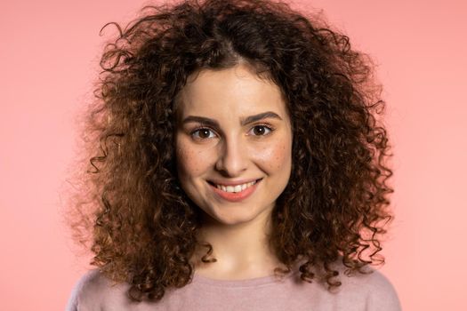 Young curly woman with trendy glitter freckles make-up. Portrait of beautiful girl on pink studio background