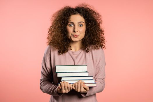 European student on pink background in studio holds stack of university books from library. Woman is happy to graduate.