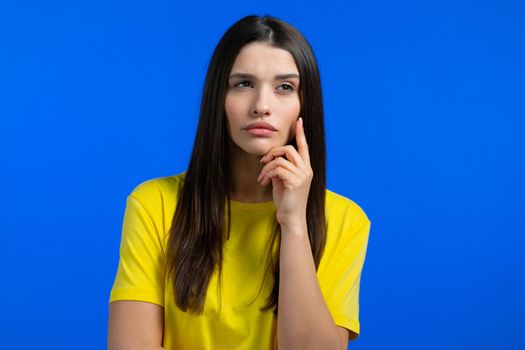 Thinking woman looking up on blue studio background. Pensive face expressions. Pretty model with attractive appearance