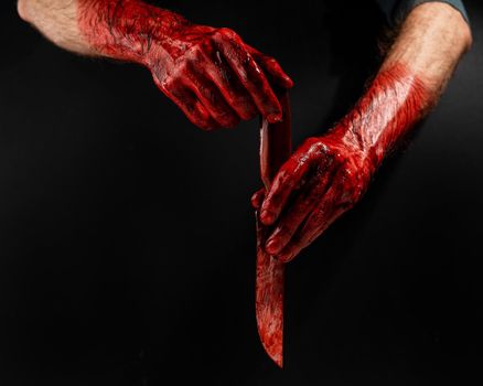 Man holding knife with bloody hand on black background.