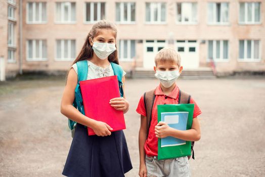 School learners of different age in front of conventional school in medical masks