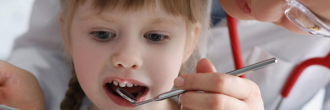 Dentist examining teeth of little girl with steel instruments in clinic