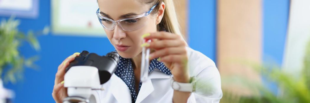 Woman scientist chemist looking through microscope and holding test tube