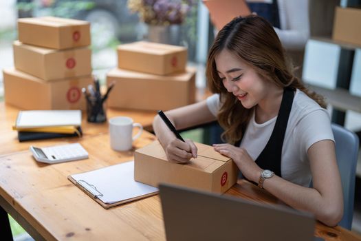 Woman running a small startup business in an office is working on a laptop and boxes for packing and preparing items for shipping.