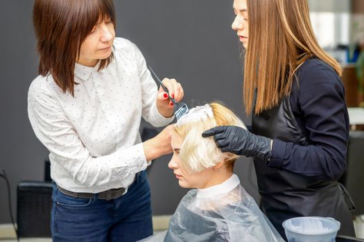 Two hairdressers dyeing hair of woman