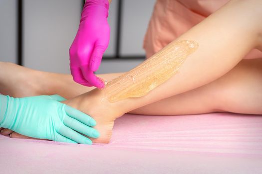 Two cosmetologists waxing woman's legs