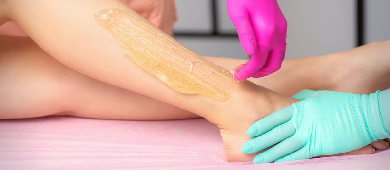 Two cosmetologists waxing woman's legs