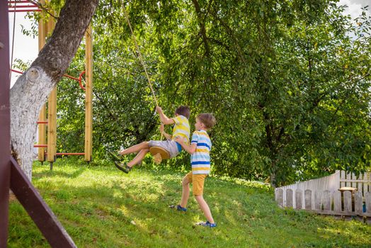Two adorable happy little boys is having fun on a rope swing which he has found while having rest outside city. Active leisure time with children
