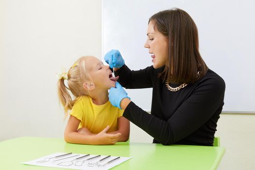 Speech therapist working with little girl in office training pronunciation
