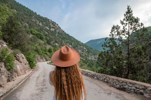 Female traveler in brown hat and white dress looking at amazing mountains and forest, wanderlust travel concept, atmospheric epic moment