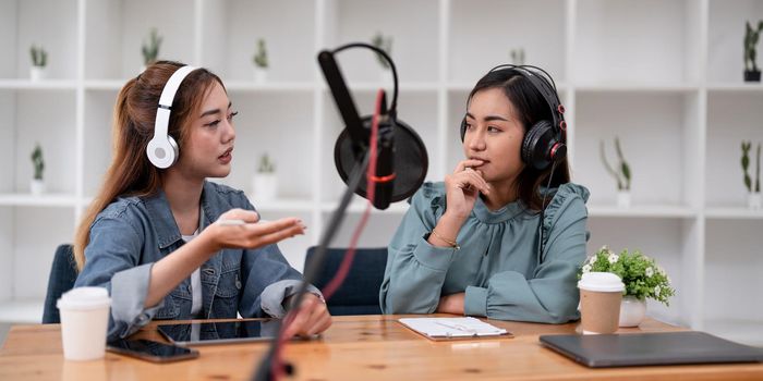 Asian female host recording radio podcast interview with guest at home office
