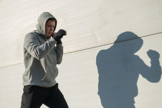 Caucasian man in hoodie is training boxing outdoors.