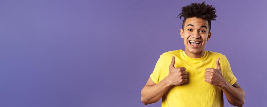 Close-up portrait of enthusiastic healthy hispanic guy staying positive, show thumbs-up and smiling, encourage people stay home, feel fine, like and approve friends plan, standing purple background