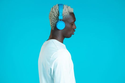 Handsome black man with trendy hairdo and headphones in studio against blue background. Music, dance, radio concept.