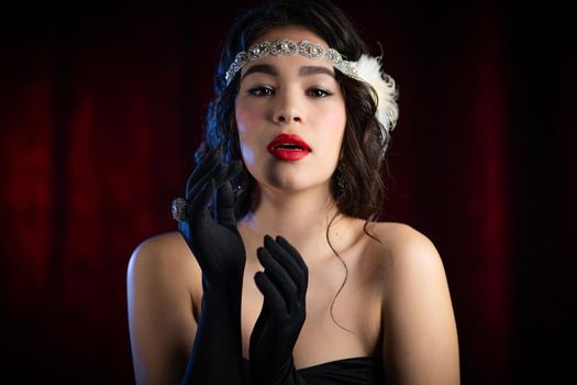 Portrait of old-fashioned brunette woman dressed in style of Gatsby era flirting and posing on burgundy velours background. Vintage, party, retro fashion concept.