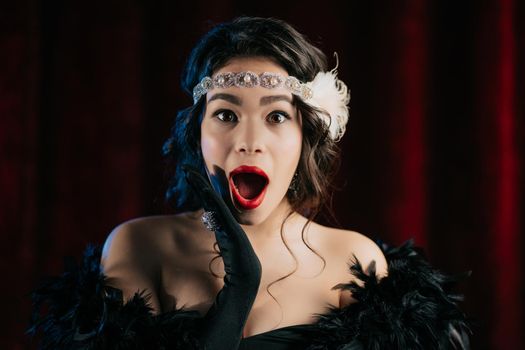 Retro styled woman dressed in Gatsby era is pleasantly surprised, shows wow delight effect gesture on dark background. Roaring twenties, retro, party, fashion concept