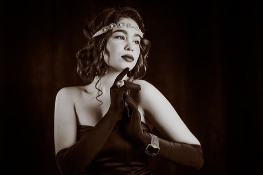 Woman dressed in Roaring twenties era with feathers boa on dark background. Retro, party, fashion concept. Sepia film effect.
